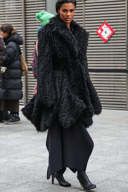 Tina Kunakey en total look noir et manteau en fausse fourrure