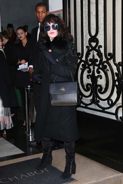 Isabelle Adjani en long manteau noir et lunettes carrées bleues