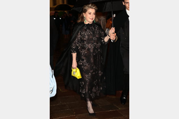 Catherine Deneuve en robe noire en dentelle et mini sac à main jaune
