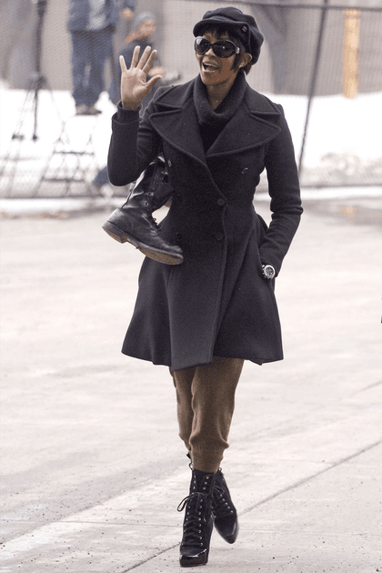 Naomi Campbell en manteau noir cintr&eacute; et pantalon kaki