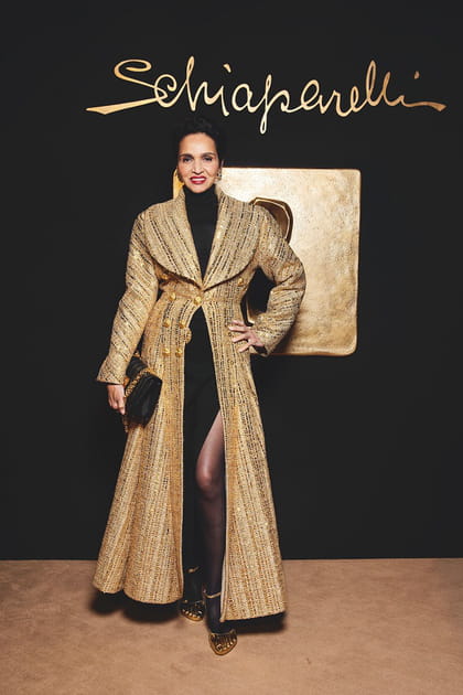 Farida Khelfa en long manteau doré texturé et sac à main matelassé au défilé Schiaparelli