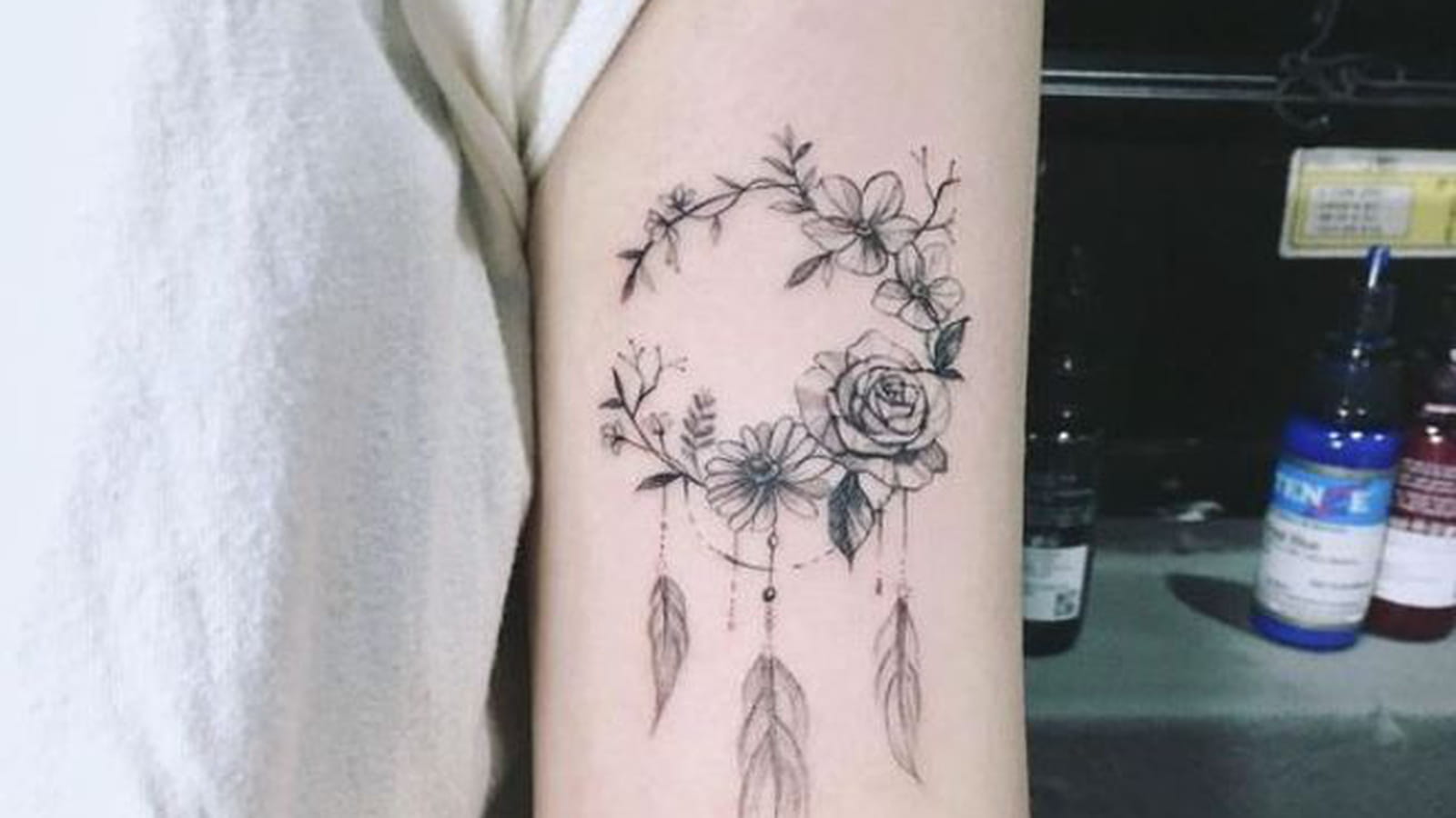 Tatouage lune fleurie et plumes sur le bras