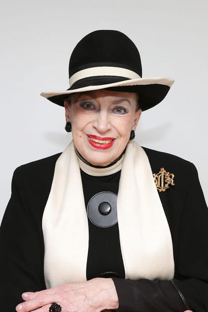 Geneviève de Fontenay en chapeau bicolore, broche dorée et écharpe blanche