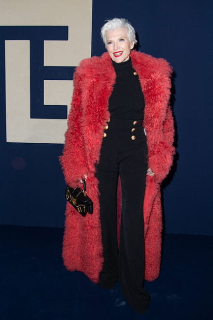 Maye Musk en longue veste rouge texturée et pantalon taille haute noir à boutons dorés au défilé Balmain