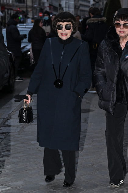Mireille Mathieu en manteau long bi-matière et mini sac à main à chaînes au défilé Pierre Cardin
