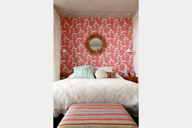 Un miroir en rotin sur du papier peint fleuri dans la chambre