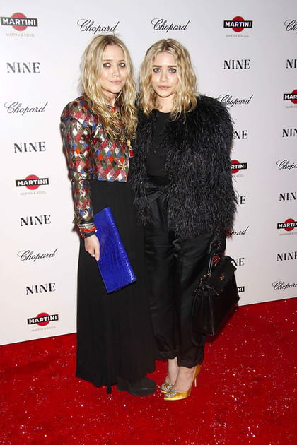 Mary Kate Olsen en jupe longue noire et veste courte colorée, Ashley Olsen en pantalon satiné noir et veste à plumes
