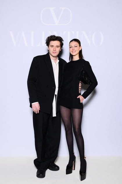 Brooklyn Beckham en pantalon large et chemise blanche et Nicola Peltz en combishort et sandales à plateformes au défilé Valentino