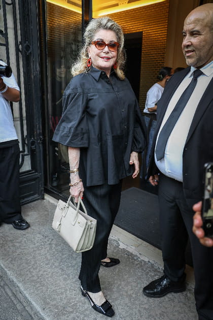 Catherine Deneuve en blouse noire, pantalon noir et sac &agrave; main cr&egrave;me