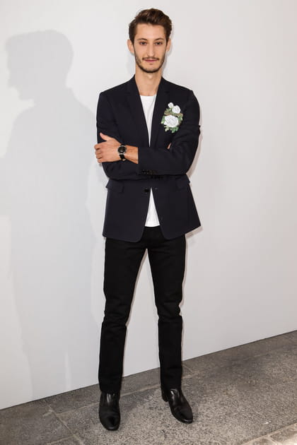 Pierre Niney en costume noir et T-shirt blanc avec détail fleuri