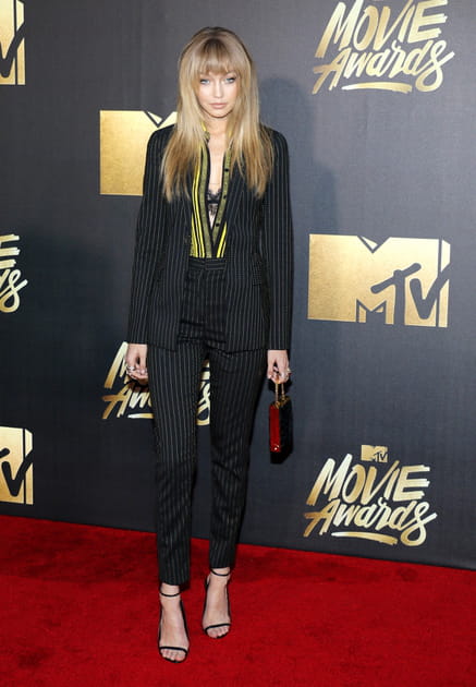 Gigi Hadid en costume noir et blouse jaune ray&eacute;e Versace