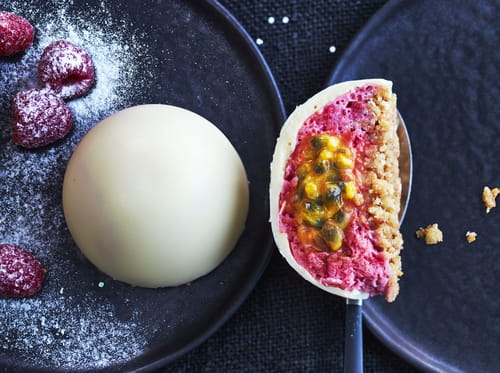 Dôme de chocolat blanc à la mousse de framboises, cœur au fruit de la passion et croquant de palet breton et pralin